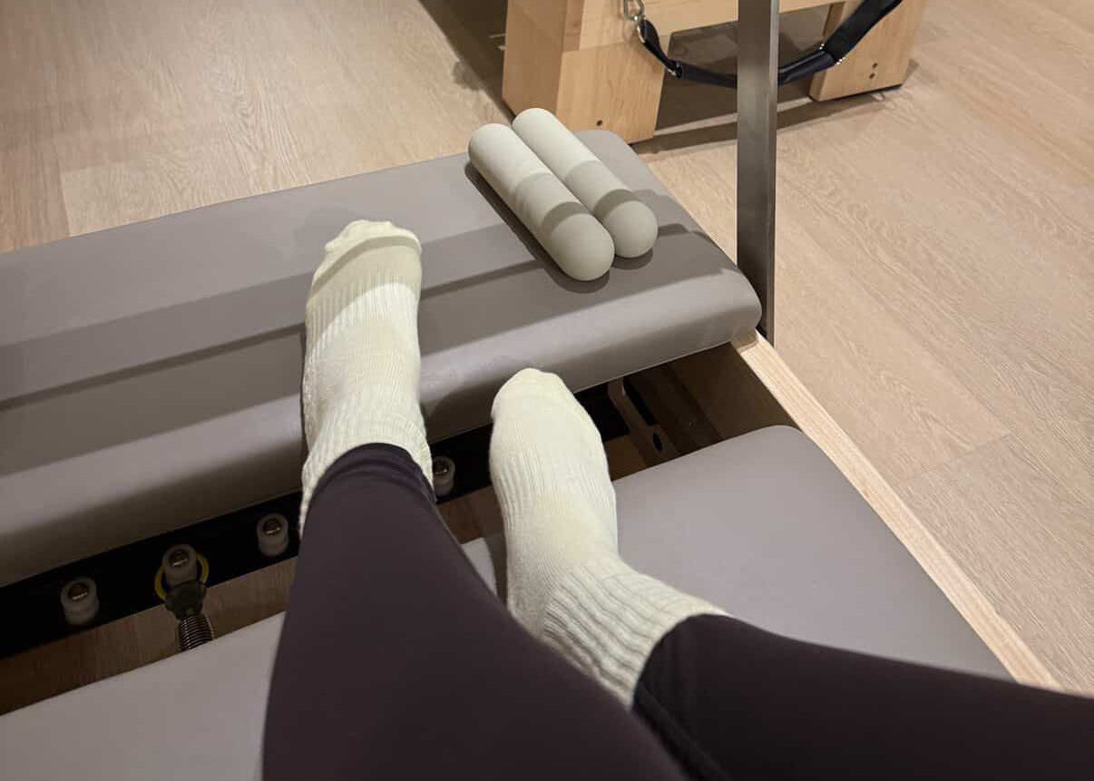 Pilates reformer machine in a Pilates studio with a person's feet on the equipment.